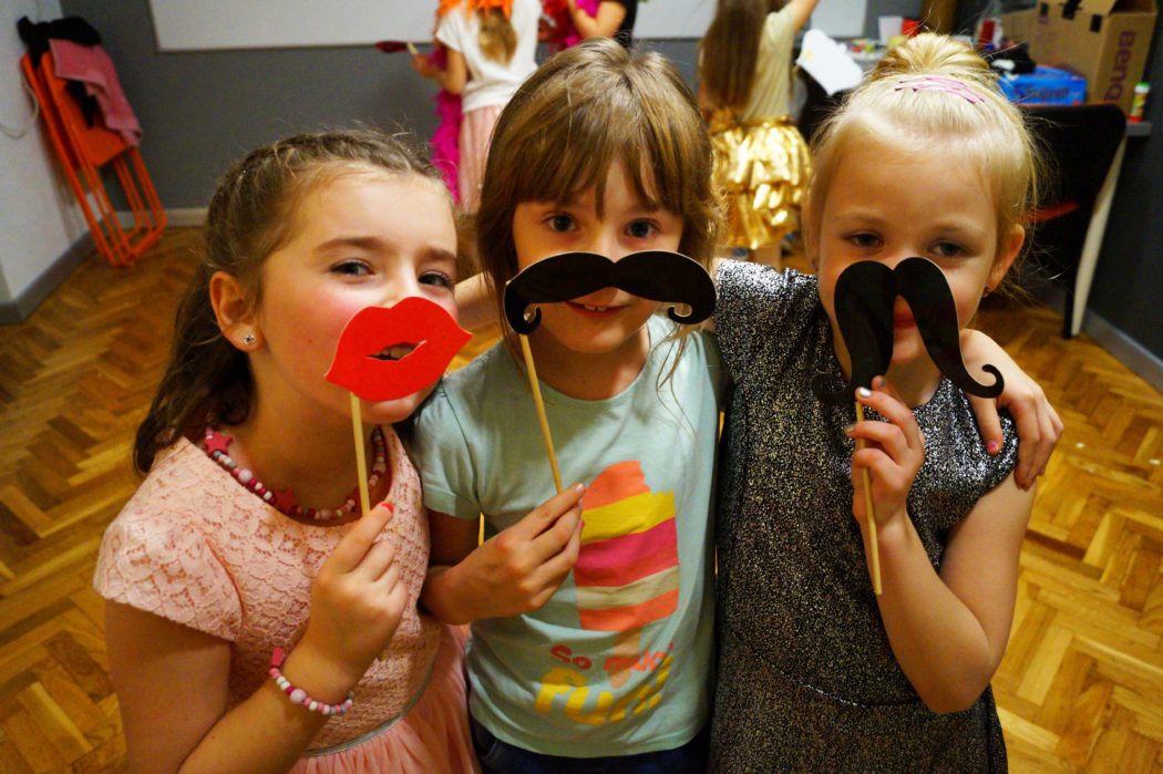 dzieci na zabawie przykładają sztuczne wąsy do twarzy