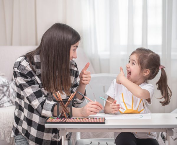 A mother with a child sits at the table and does homework. The child learns at home. Home schooling.